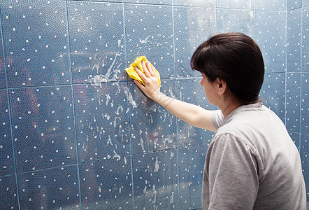 女人用布衣罩洗墙壁的瓷砖图片