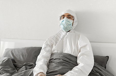身穿保护性白色西装和面罩的人的肖像 他们因为2019年风湿而坐在卧室的床上 等待冠状病毒检疫结束 自我隔离风险肺炎面具睡衣防护服图片