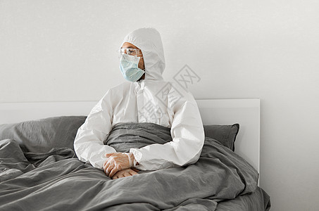 身穿保护性白色西装和面罩的人的肖像 他们因为2019年风湿而坐在卧室的床上 等待冠状病毒检疫结束 自我隔离感染疾病成人商务流感压图片