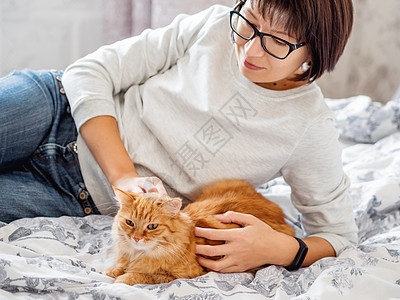 可爱的姜猫和戴眼镜的女人躺在床上 女人在摸她的毛绒宠物 早安毯子眼镜投标卧室女性女士情感时间猫科动物就寝图片