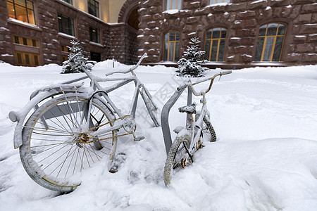 两辆脚踏车被绑在门外的架子上 雪降时下雪覆盖着积雪图片