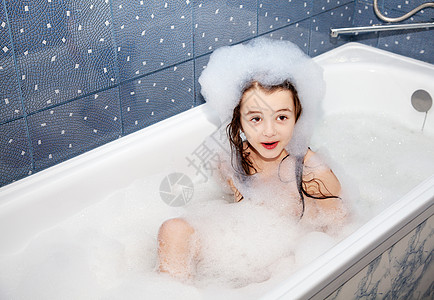 坐在浴缸里带着肥皂糖的小女孩惊讶地坐着图片