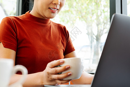 亚洲妇女在打笔记本电脑键盘时端着咖啡杯互联网商务桌子工作女士咖啡技术商业办公室女性图片
