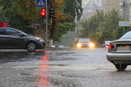 红灯照亮了人行道和沥青路上的大雨水坑路口反射红绿灯建筑物水域路面下雨住宅波纹图片