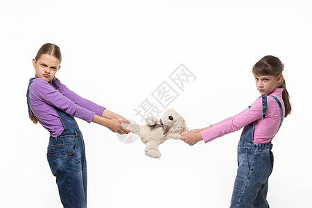 两个心怀不满的姐妹 在一个白色背景上分享一个玩具图片