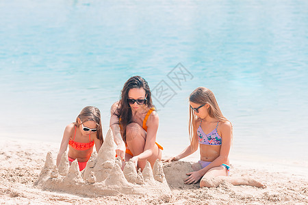 母亲和小女儿在热带海滩建造沙滩城堡海滨海洋孩子喜悦家庭假期闲暇女士女孩快乐图片