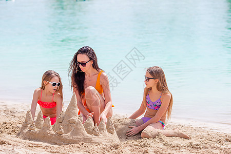 母亲和小女儿在热带海滩建造沙滩城堡海岸女孩游泳衣海滨女士喜悦玩具海岸线海洋沙堡图片