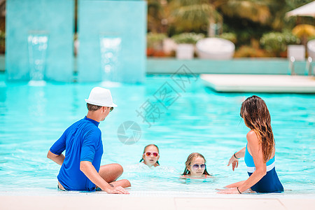 有两个孩子的年轻家庭在户外游泳池享受暑假飞溅游泳水池活动女儿成人闲暇女孩假期男人图片