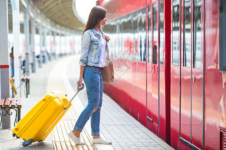 在火车车站带行李的年轻天主教女孩乘火车旅行飞机手提箱铁路车皮平台女性红色列车旅游木板图片