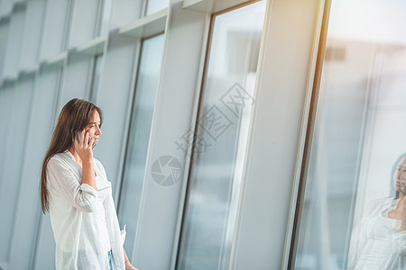 在机场用手机和登机护照进行电话交谈的女游客飞机旅行假期经理女性乘客飞行技术人士笔记本图片