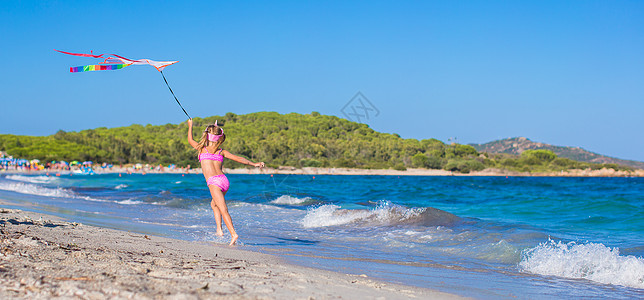 快乐的小女孩在热带海滩上带着飞风筝跑来跑去图片
