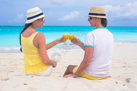 在热带海滩上带橙汁杯的快乐情侣图片