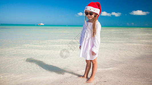 热带海滩上戴着红色圣诞老人帽子的小可爱女孩婴儿乐趣异国季节假期幸福游泳友谊童年支撑图片