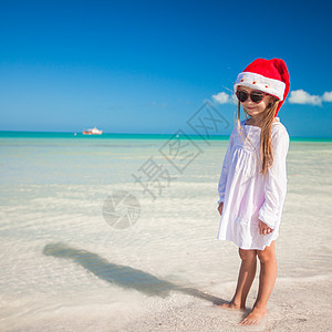 热带海滩上戴着红色圣诞老人帽子的小可爱女孩幸福童年明信片支撑婴儿友谊情调假期戏服闲暇图片