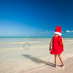 热带海滩上戴着红色圣诞老人帽子的小可爱女孩乐趣婴儿季节假期戏服海岸情调姐姐朋友幸福图片