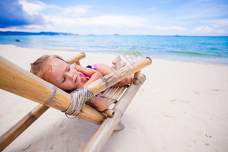 可爱的小女孩在暑假期间 在沙滩用多彩色木椅放松图片
