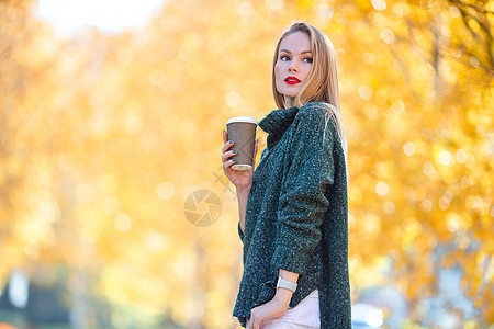秋瀑概念  美丽的女人在秋公园喝咖啡 在秋天的树叶下金发女郎外套拿铁饮料快乐木头季节杯子咖啡叶子图片