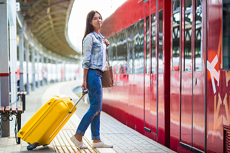 在平台上带着行李的年轻女孩 等待Aero表达式运输航程木板旅行游客铁路速度车皮车站女性背景图片