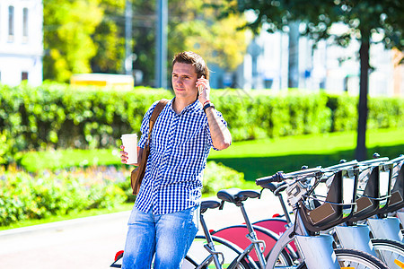 在户外自行车上喝咖啡的年轻人微笑蓝色闲暇电话生活咖啡男性男人太阳镜玻璃图片