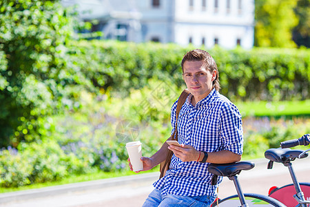 在户外自行车上喝咖啡的年轻人运动电话男人早餐享受细胞饮料蓝色生活太阳图片