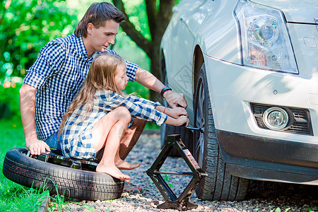 可爱的小女孩坐在轮胎上 帮助父亲在美丽的夏日 换户外车轮 让父亲更衣图片
