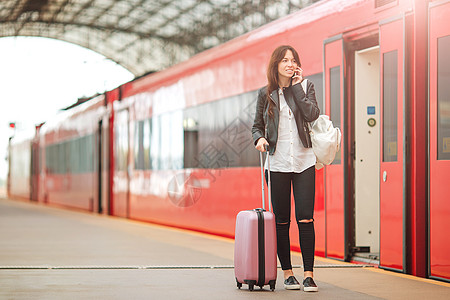 旅游客服素材携带行李的年轻女子在火车站用手机交谈 她旅行时乘快车等候客服旅游者 笑声乘客铁路火车电话旅游游客车站平台车皮速度背景