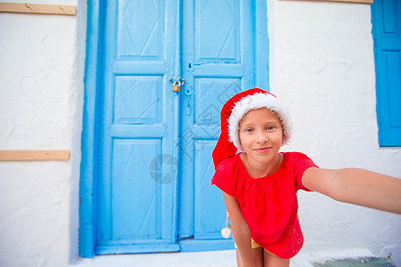 Santa Hat的可爱小女孩在希腊村狭窄街道上自拍图片