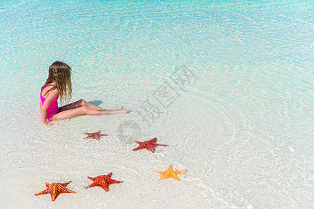 在白空沙滩上水中有海星的可爱小女孩图片