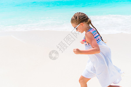 Caribbean度假期间在海滩上穿白裙子的可爱小女孩幸福海岸线海景支撑冒险沿海帽子情感异国游客图片