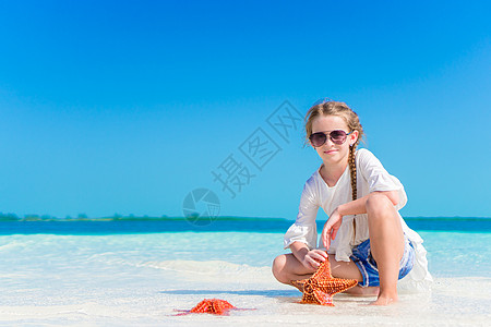 可爱的小女孩 海星在白空海滩上孩子动物群眼睛游客喜悦海岸线热带微笑海滨旅行图片