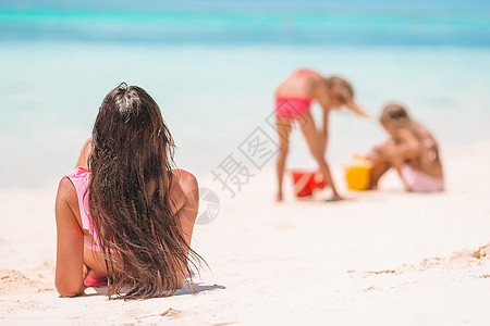 母亲和小女儿在热带海滩建造沙滩城堡海洋玩具海岸父母享受异国家庭喜悦游泳衣女孩图片