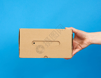 手手里拿着一盒蓝色背景的棕色纸纸箱货运贮存送货纸盒工艺正方形商业纸板邮件运输图片