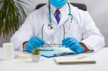 穿白大衣和蓝色乳胶手套的男男性医生坐在Whit桌子眼镜医师医院治疗专家实验室保健卫生职场背景图片
