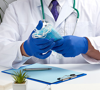穿着白大衣和蓝色乳胶手套的医生坐在工作室实验室职业全科面具治疗绷带工作男性桌子图片