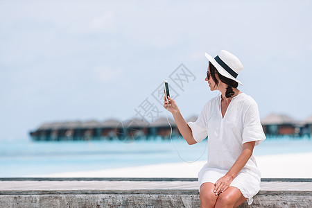 在热带沙滩度假期间 青年妇女通过电话交谈技术闲暇消息旅游旅行手机漫游奢华海洋细胞图片