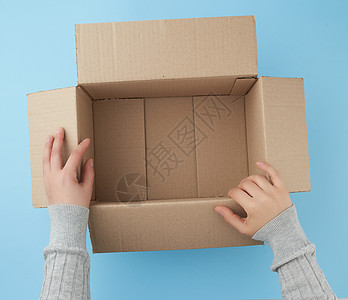 女性手握着一盒空开的棕色纸板材料运输商业店铺蓝色仓库包装邮件纸盒贮存图片