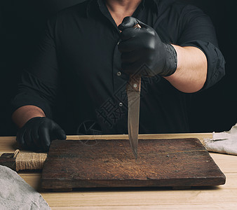 穿黑色衬衫和黑乳胶手套的厨师拿着大便服屠夫木板锐化金属刀刃手臂用具男人成人工作室图片
