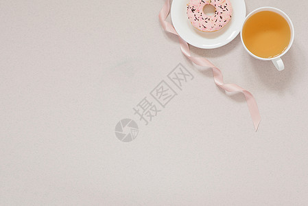 极简主义横幅咖啡休息时间 白瓷杯中的绿茶 白盘中的粉色甜甜圈 灰褐色背景中的粉色缎带 带复制空间图片