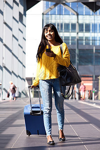 携带袋子和移动电话在车站行走的印度年轻妇女图片