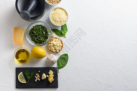 罗勒酱意大利香蒜酱的不同成分 磨碎的帕尔马干酪 罗勒叶 松子 橄榄油 大蒜在白色石板侧顶视图上 侧面文字空间图片