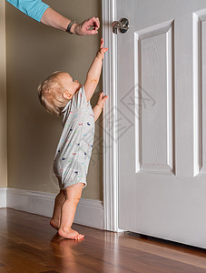 刚能走路的小婴儿伸手去拿木地板上的门把手孩子女士成人房子脚尖房间监视器童年手表安全图片