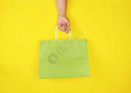 手持绿色纸袋和黄色背角的女用手图片