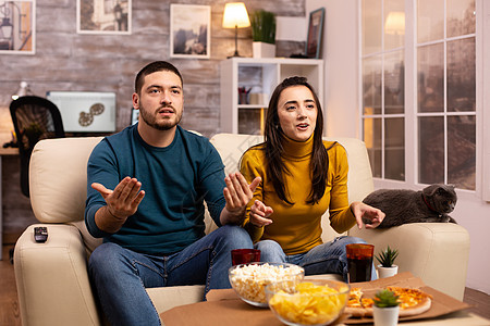 情侣在看电视时为他们最爱的团队欢呼爆米花成人男人公寓男性扇子闲暇手表娱乐沙发图片