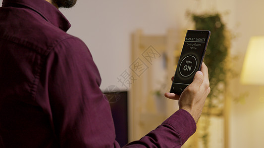 一个人拿着智能手机 有语音激活功能的智能灯光应用程序 可以打开家里的灯图片