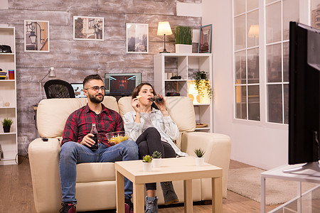 坐在沙发上 看电视电影的一对快乐的年轻夫妇长椅程序电视节目筹码专注娱乐房间恋人男人夫妻图片
