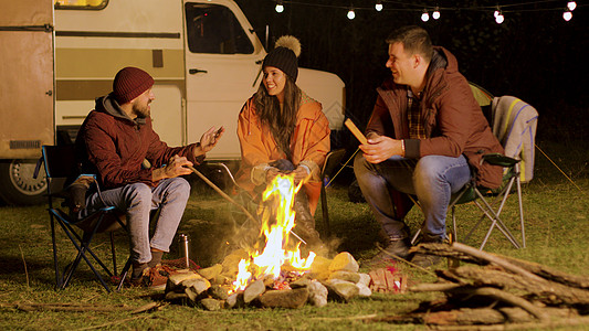 胡子人跟朋友说一个有趣的笑话 在营火周围灯泡乐趣空气营地房车露营旅游团体帐篷朋友们图片
