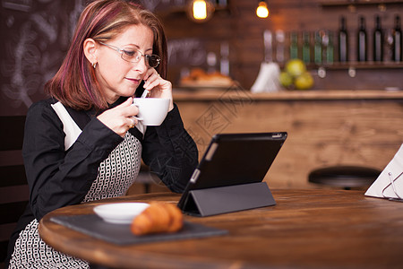 商业女商务人士一边看平板电脑一边在电话上聊天 一边说话工具时间网站咖啡女士咖啡店互联网休息企业家女性图片