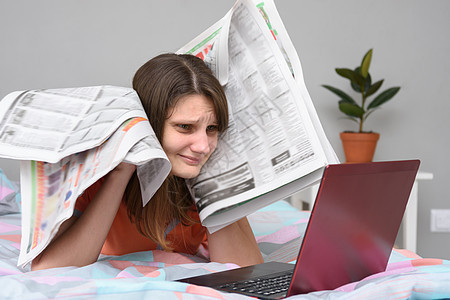 女孩把报纸放在头顶上 看着笔记本电脑屏幕寻找工作图片