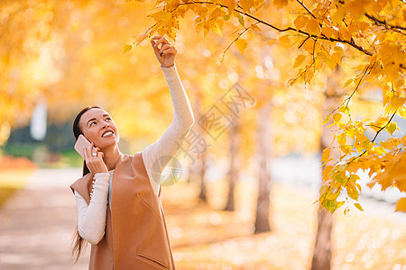 秋瀑概念  美丽的女人在秋公园喝咖啡 在秋天的树叶下快乐女士饮料木头女孩公园手机外套季节叶子图片