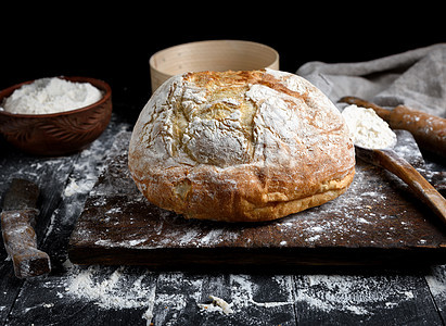 在棕色木板上烤圆白小麦面包砧板餐巾勺子食物面粉厨房黑色白色面团产品图片